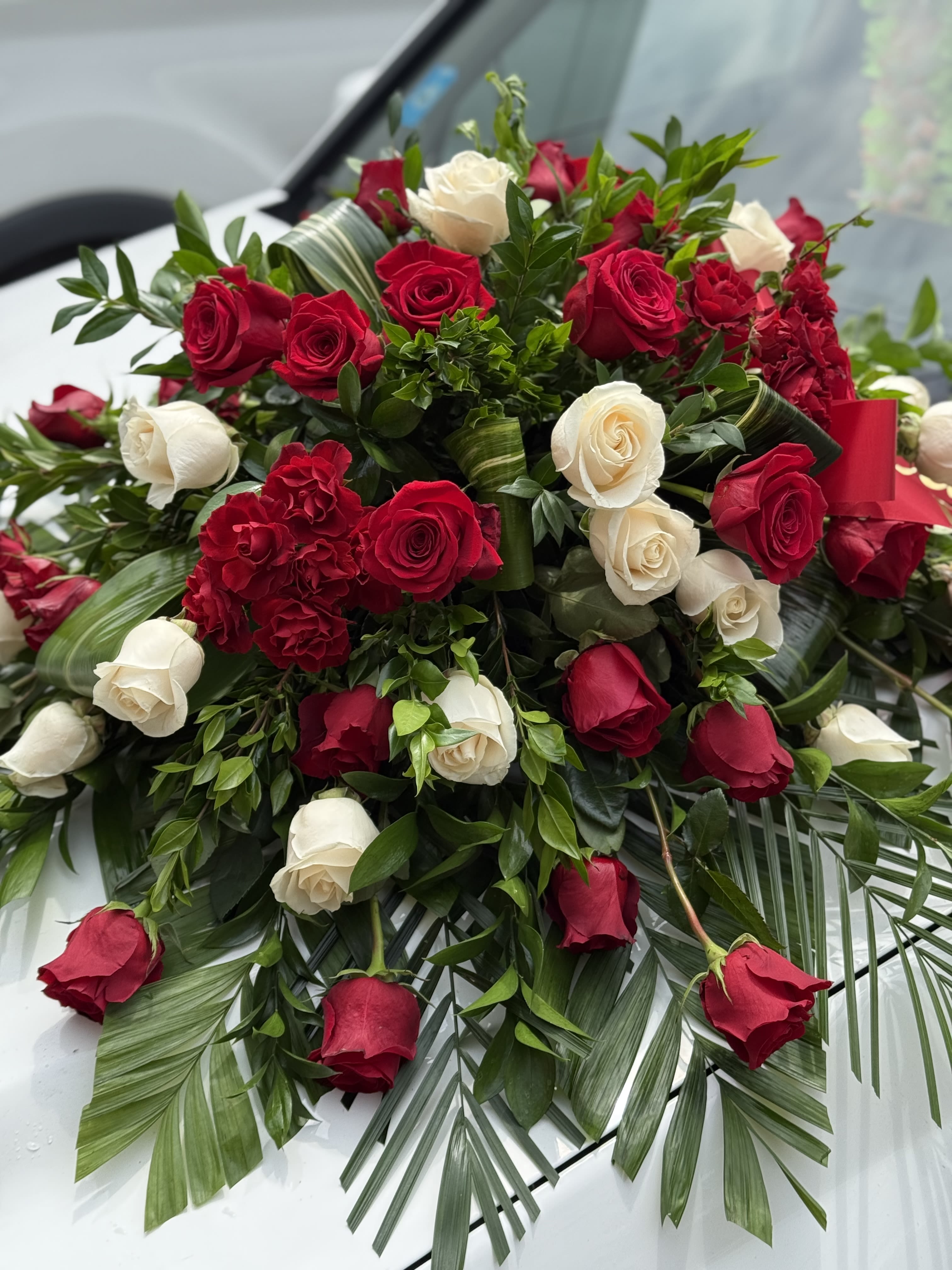 Red and white roses arranged with greenery and palm fronds