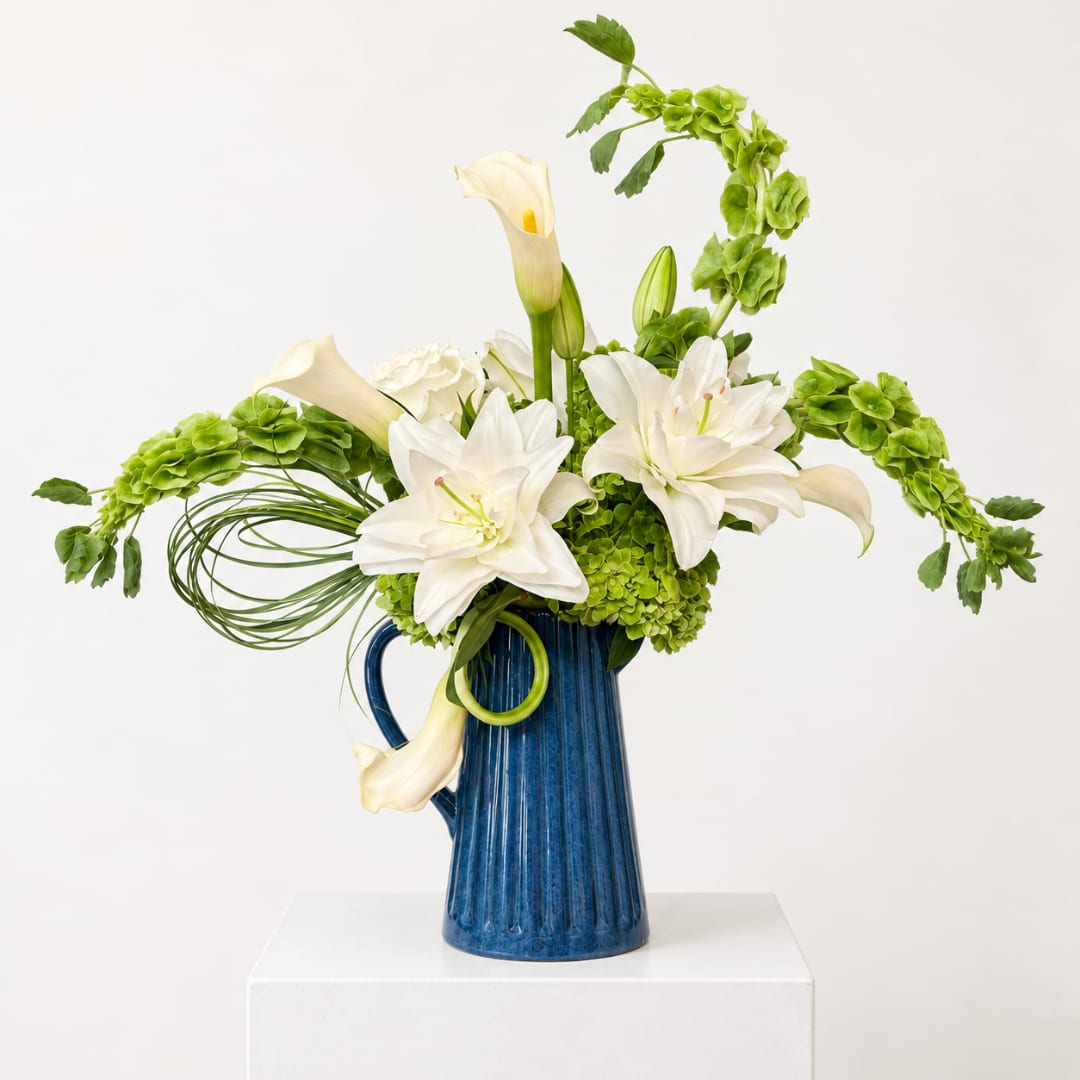 White lilies and green flowers in a blue pitcher vase