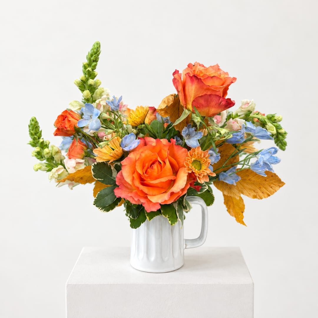 Orange and blue mixed bouquet in a white mug vase