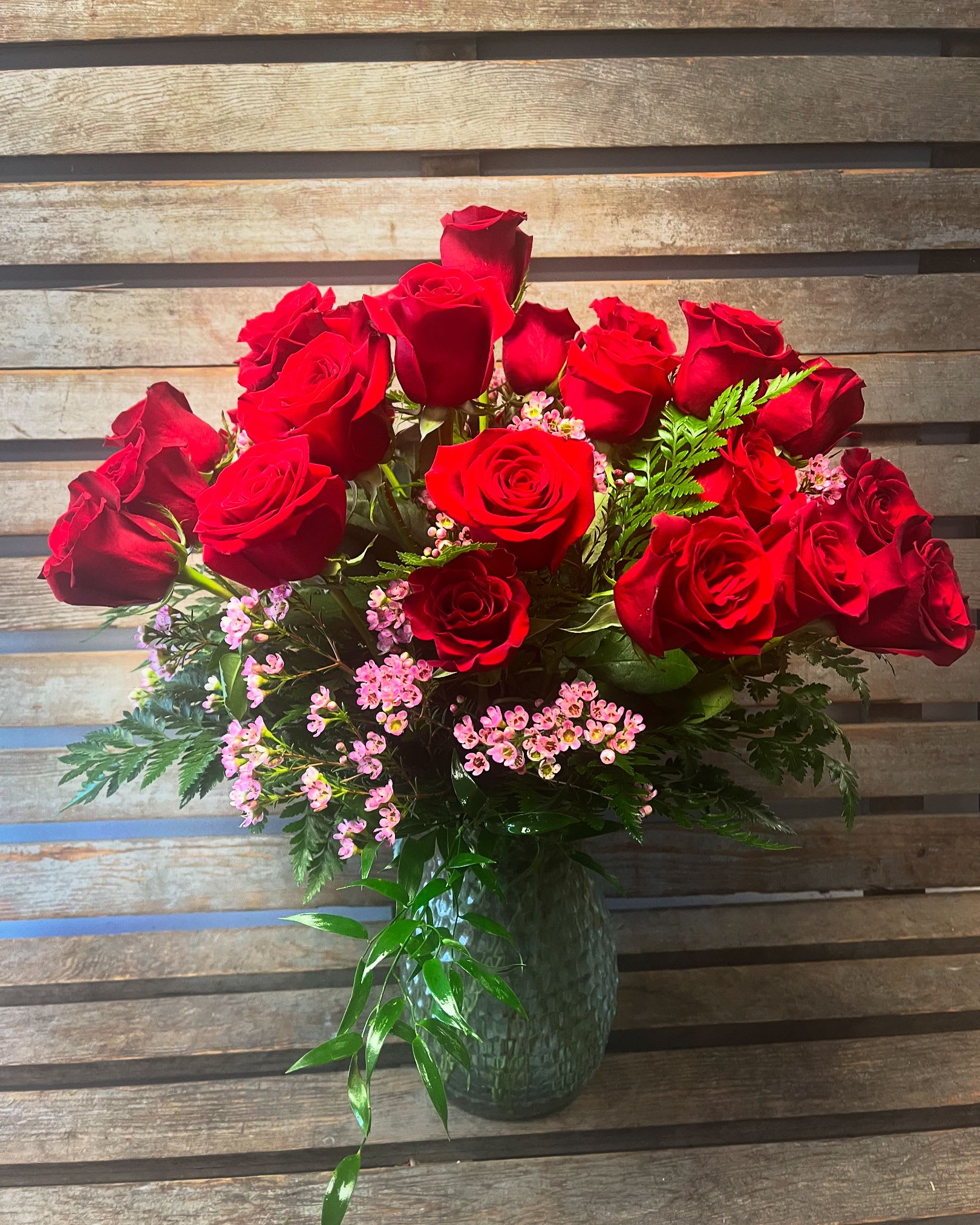 Red roses arranged in a glass vase with pink filler flowers