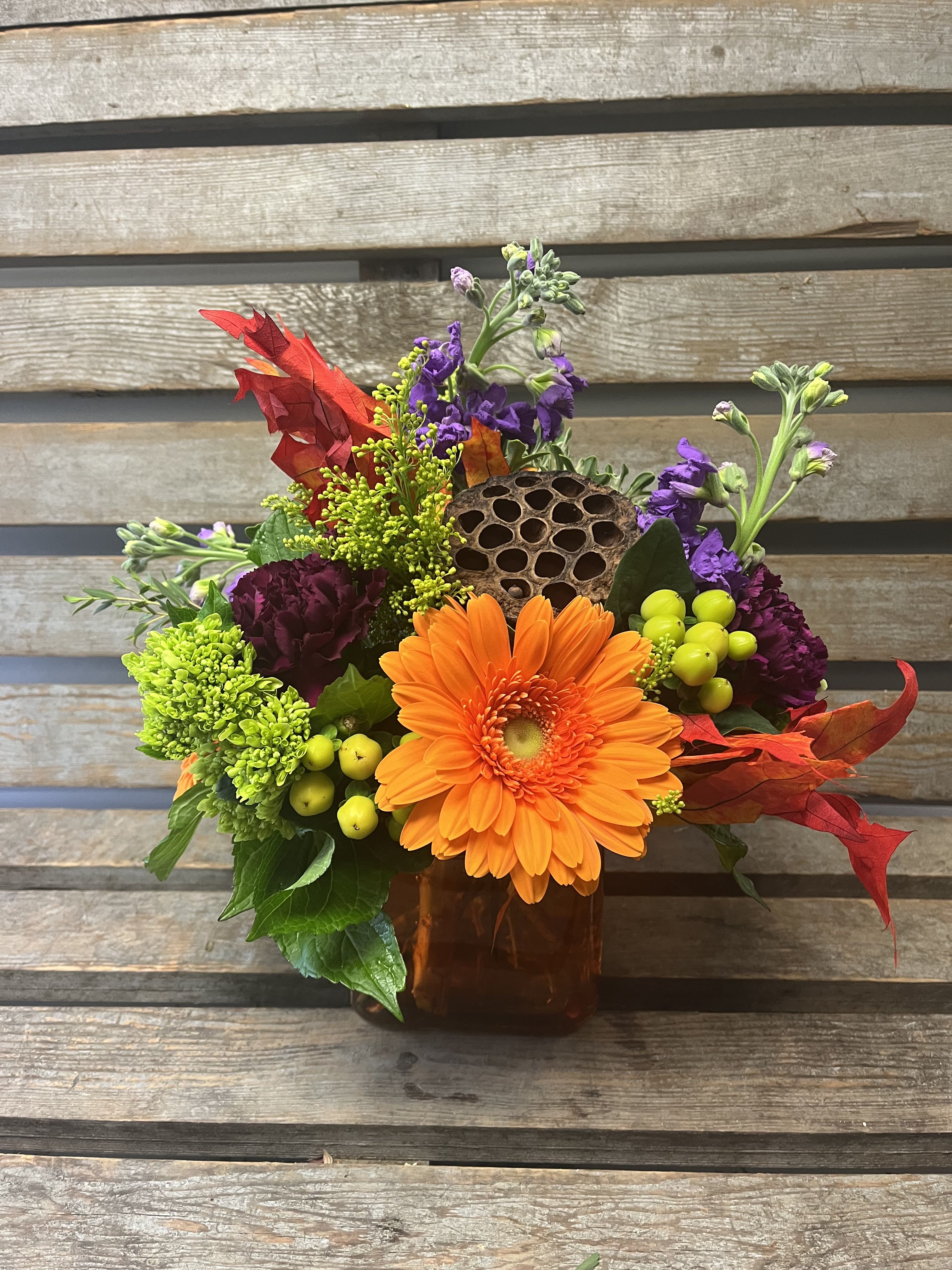Orange gerbera bouquet in a square vase with purple and green accents