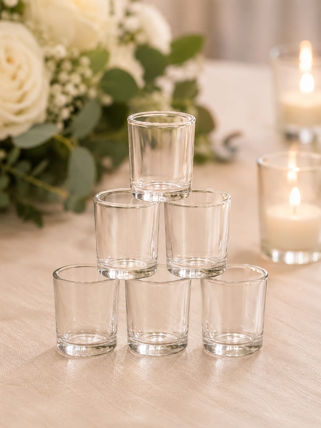 Olivia Votives - The most memorable event spaces aren’t created with bigger decorations—they’re created with layers of thoughtful details that make guests feel something the moment they walk into the room. Olivia Votive Candle Holders bring warmth, sparkle, and romantic candlelight to your celebration, helping transform ordinary tables into beautifully curated gathering spaces.  Their timeless clear-glass design complements virtually any wedding style, from rustic barn receptions and garden parties to elegant ballroom celebrations and modern events. Tuck them among floral centerpieces, greenery, lanterns, compotes, and pillar candles to create depth, dimension, and the soft glow that makes a room feel welcoming and unforgettable.  Perfect for sweetheart tables, guest tables, cocktail hours, welcome displays, cake tables, and reception décor, Olivia Votives blend effortlessly into your overall design while adding the finishing touch that ties everything together. Whether used alone or mixed with other candle holders of varying heights, they help create the layered, professionally styled tablescapes seen in today’s most beautiful weddings and events.  Because great design isn’t about filling a room with décor—it’s about creating an atmosphere your guests will remember long after the last dance.