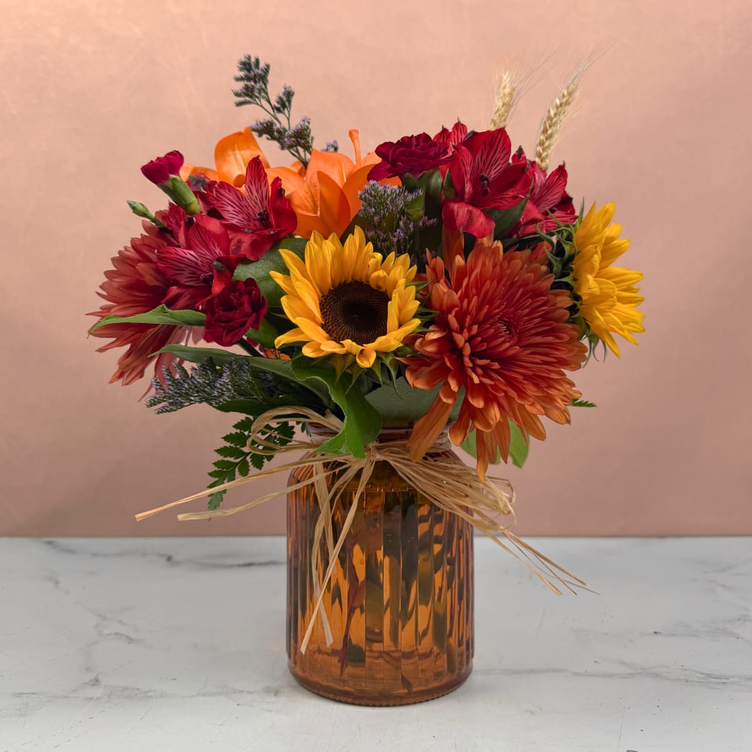 Mixed bouquet with sunflowers, orange and red blooms in an amber glass vase