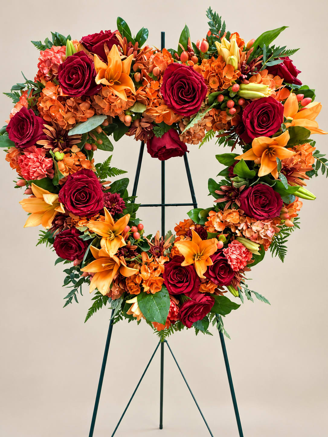 Heart-shaped floral wreath with red roses, orange lilies, and orange hydrangeas on an easel