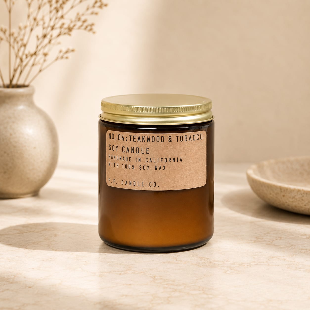 Amber jar candle with a gold lid and label reading teakwood and tobacco