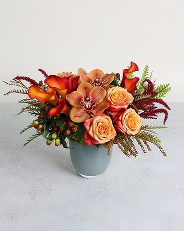 Orange calla lilies and peach roses in a light blue vase
