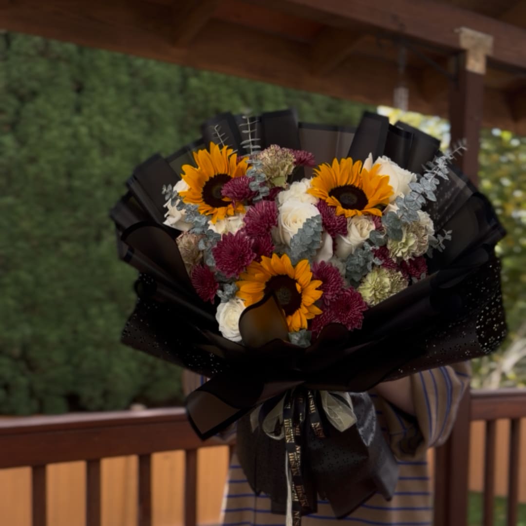 Bouquet of sunflowers, white roses, and purple flowers wrapped in black paper