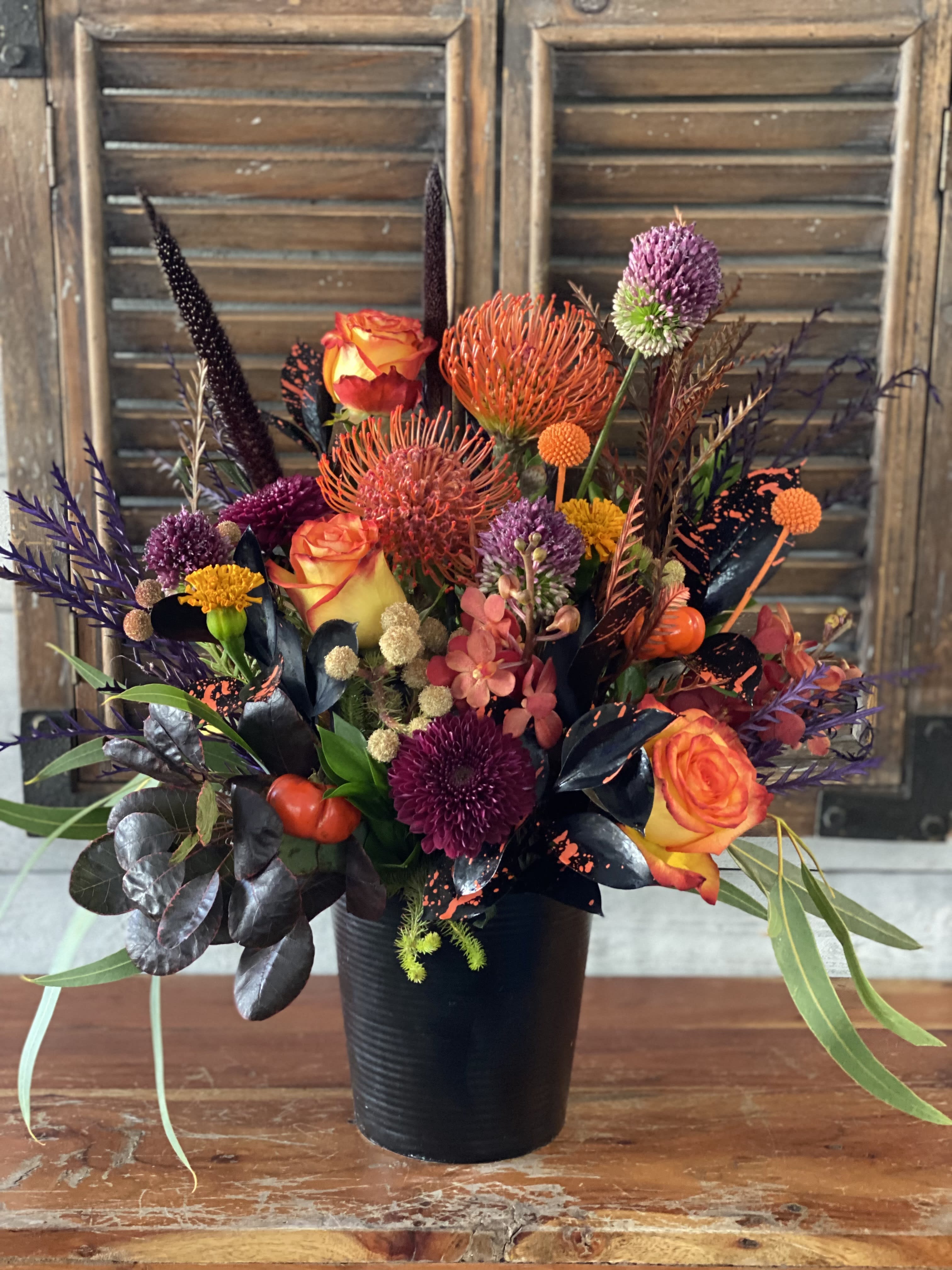 Colorful floral arrangement in a black vase with orange roses and purple blooms