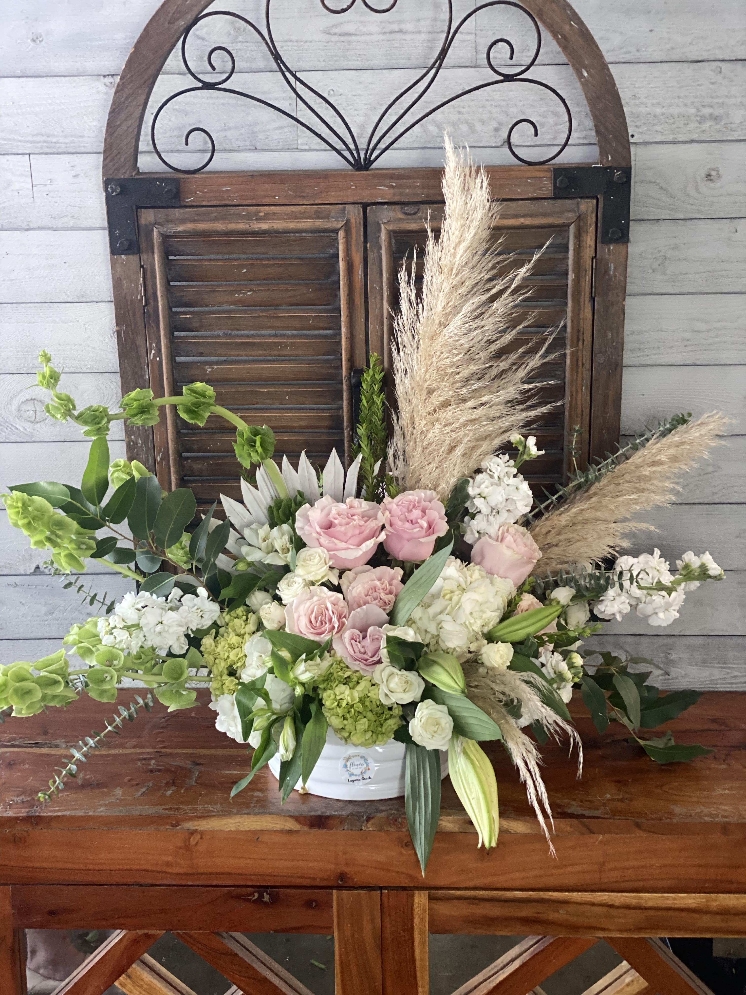 Arrangement of pink and white flowers in a white container with pampas grass