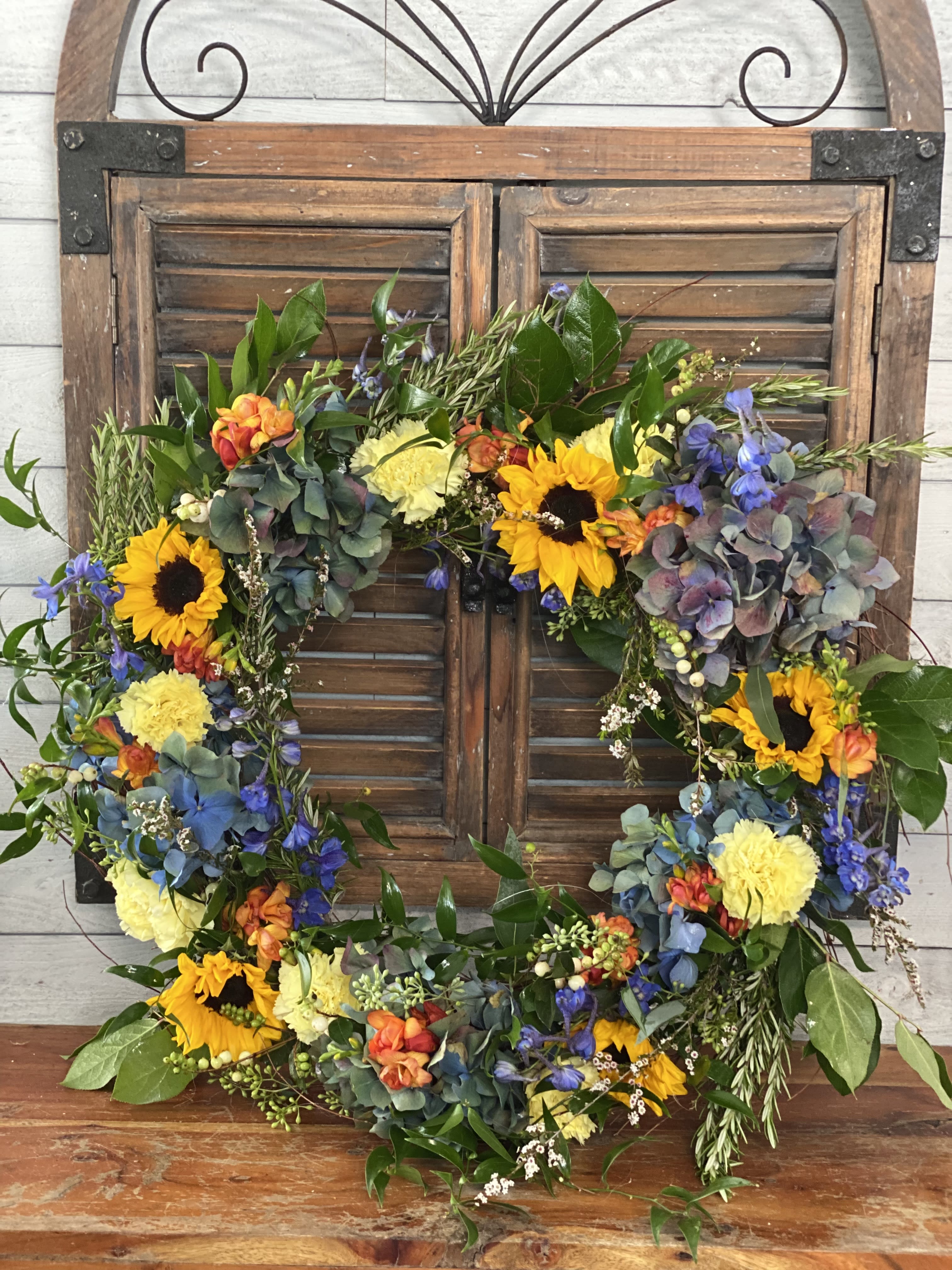 Floral wreath with sunflowers, blue blooms, and yellow carnations on a wooden shutter