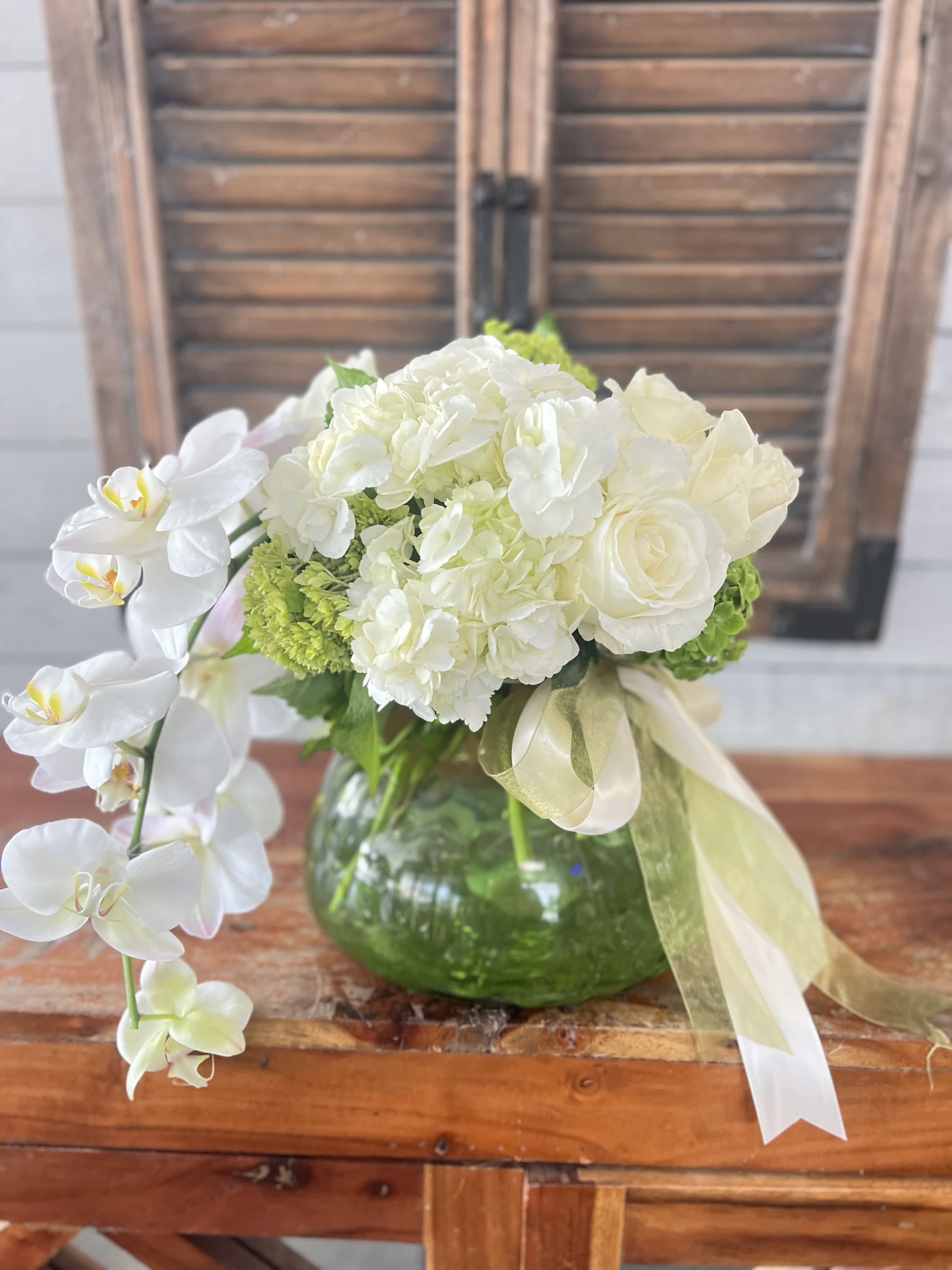 White orchid and rose arrangement in a green glass vase with ribbon