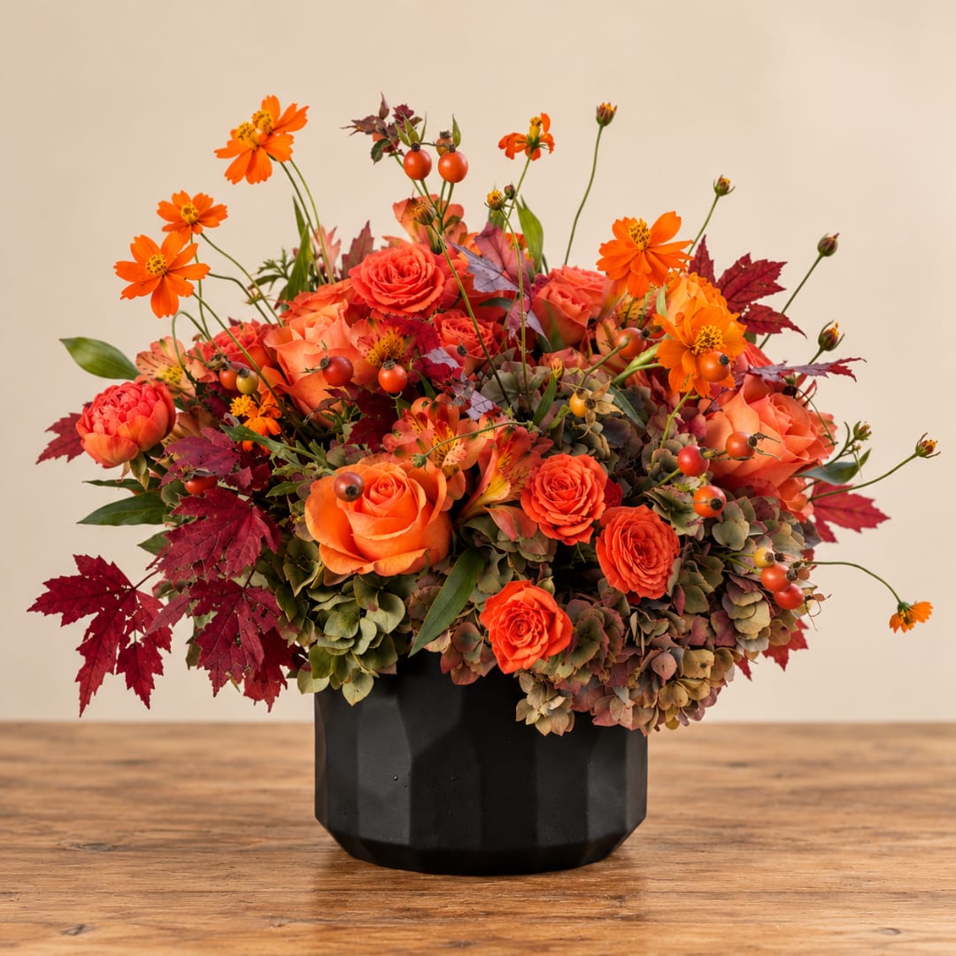 Orange roses and cosmos in a black vase with autumn leaves
