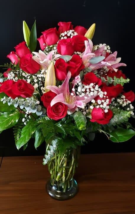 Tall glass vase of red roses, pink lilies, and white filler flowers in a full rounded bouquet