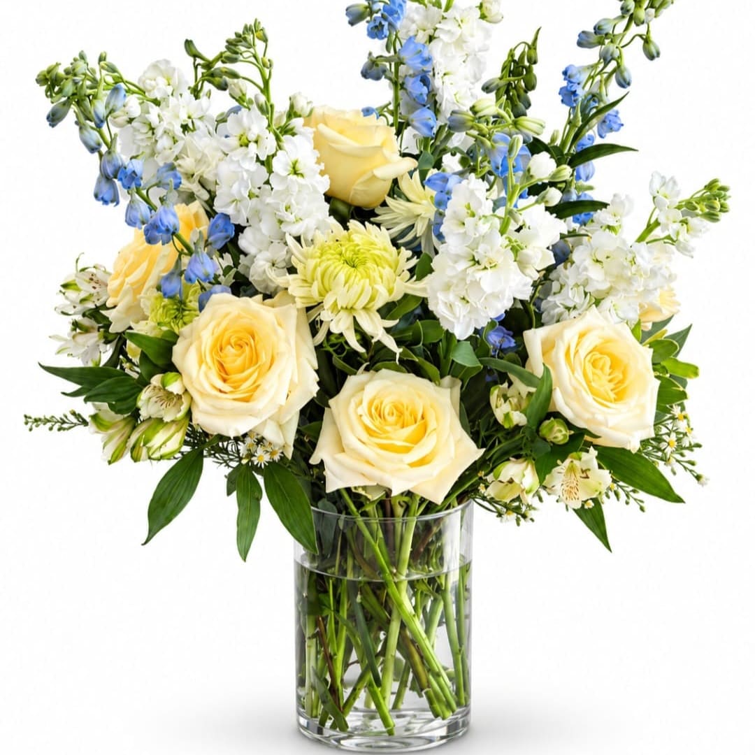Bouquet of pale yellow roses, white blooms, and blue flowers in a glass vase