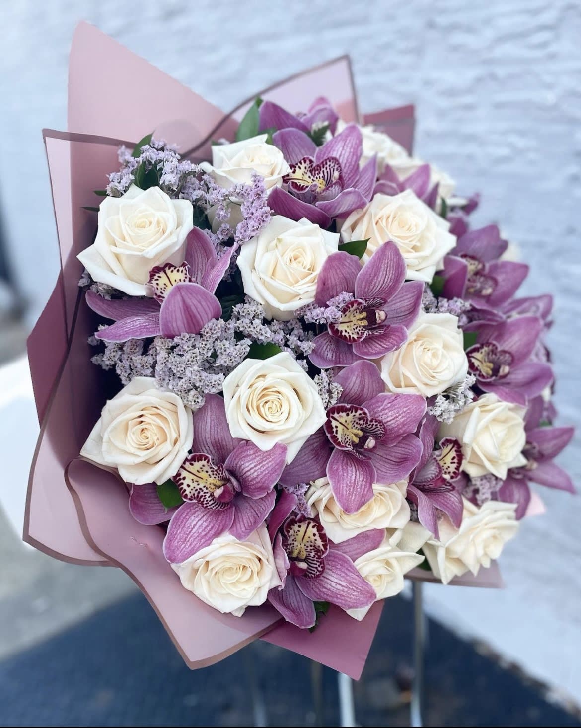 Bouquet of white roses and purple orchids wrapped in pink paper