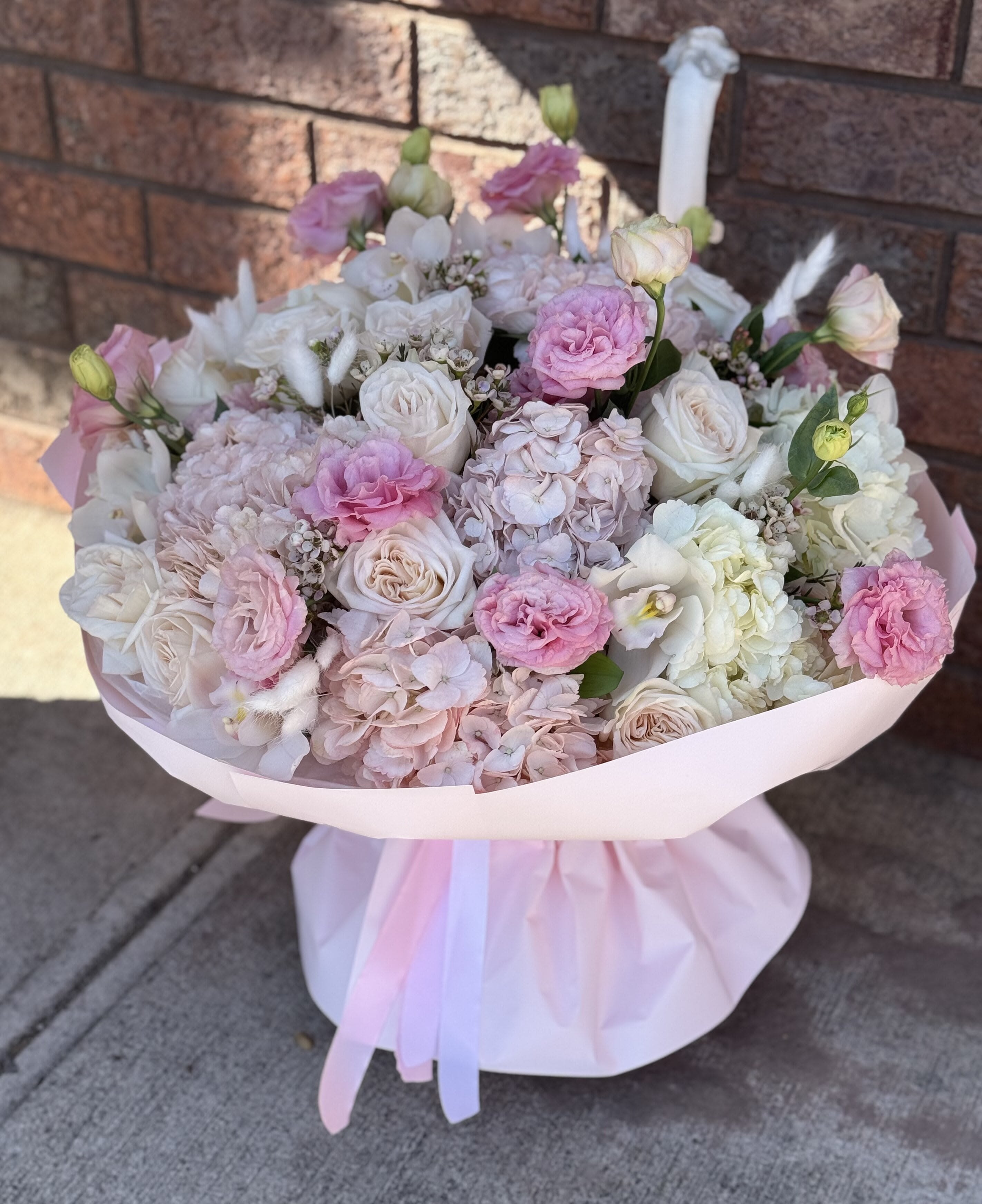 Pink and white bouquet of roses, hydrangeas, and carnations wrapped in pale pink paper