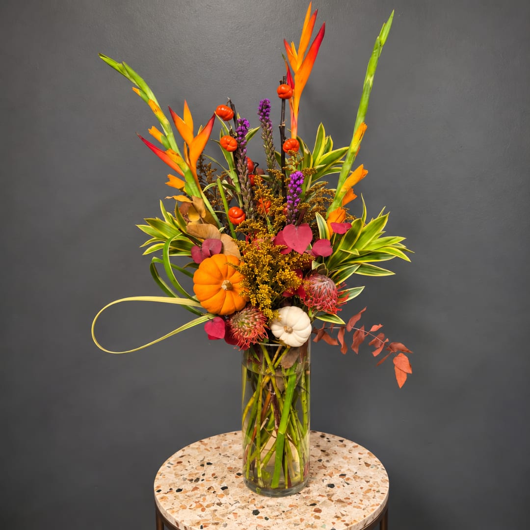 Tropical floral arrangement in a tall glass vase with orange and purple accents