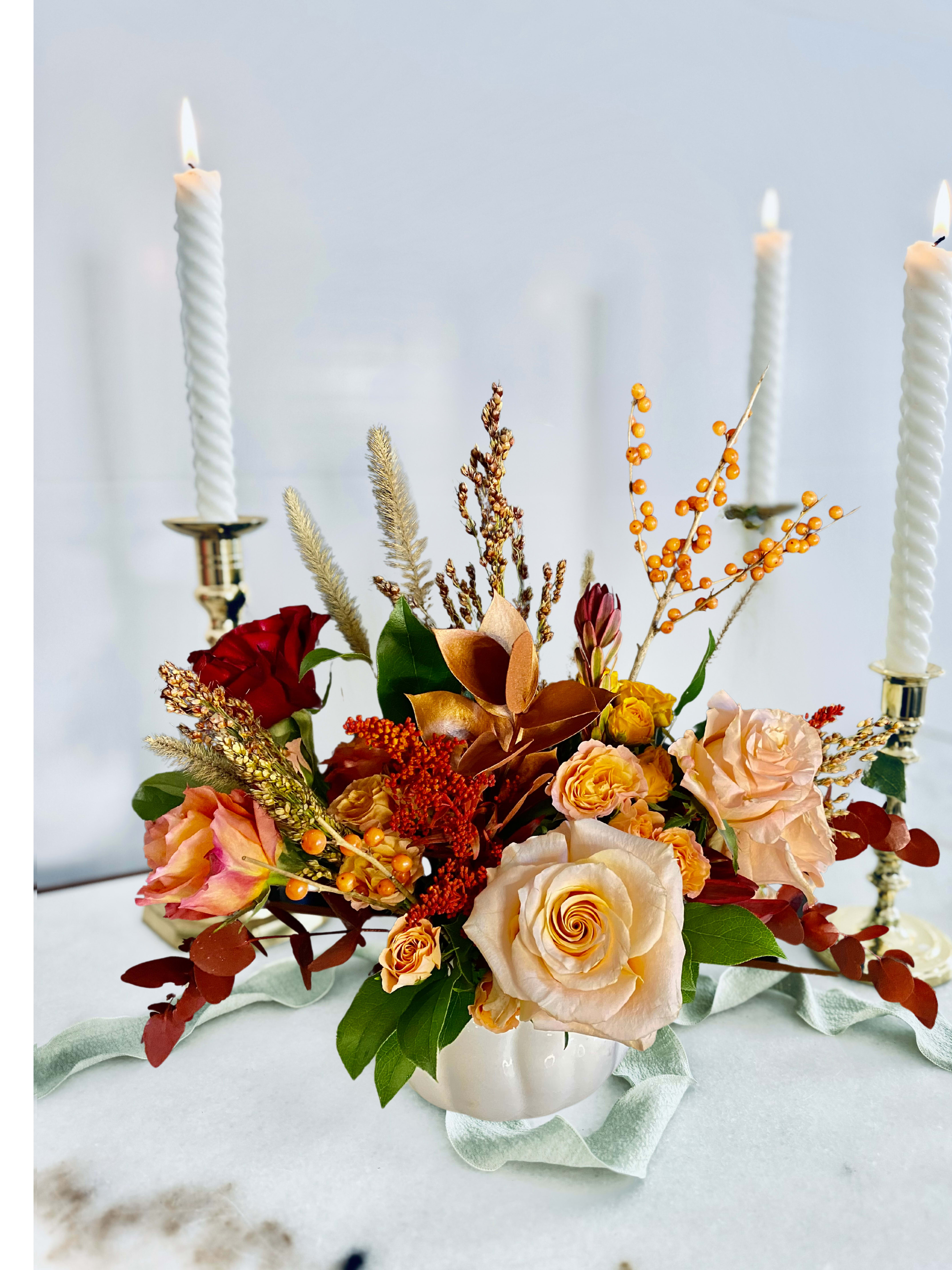 Autumn floral centerpiece with roses in a white vase and lit candles