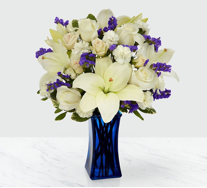 White lilies and roses with purple filler in a blue glass vase