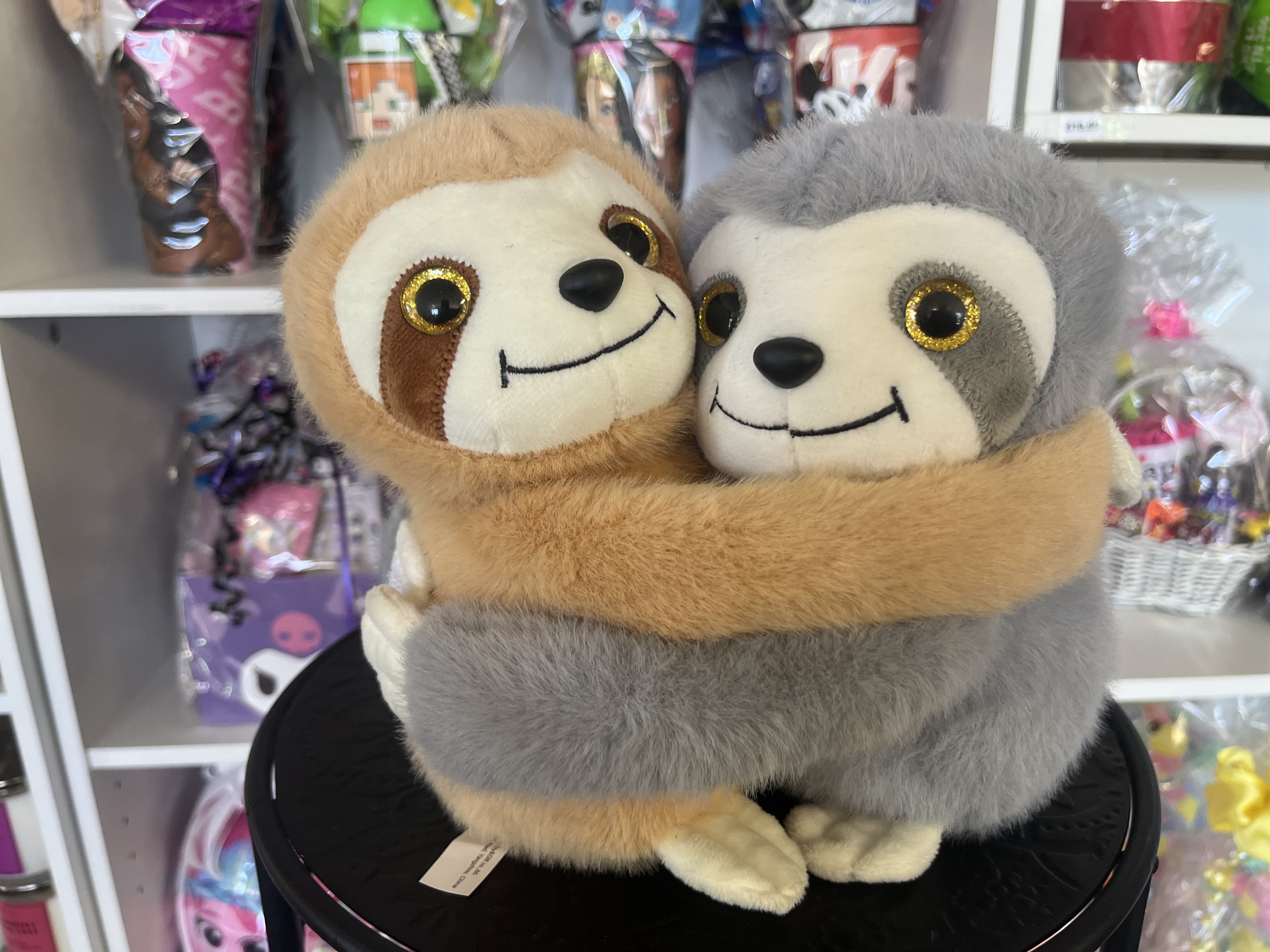 Two plush sloths hugging on a black display stand