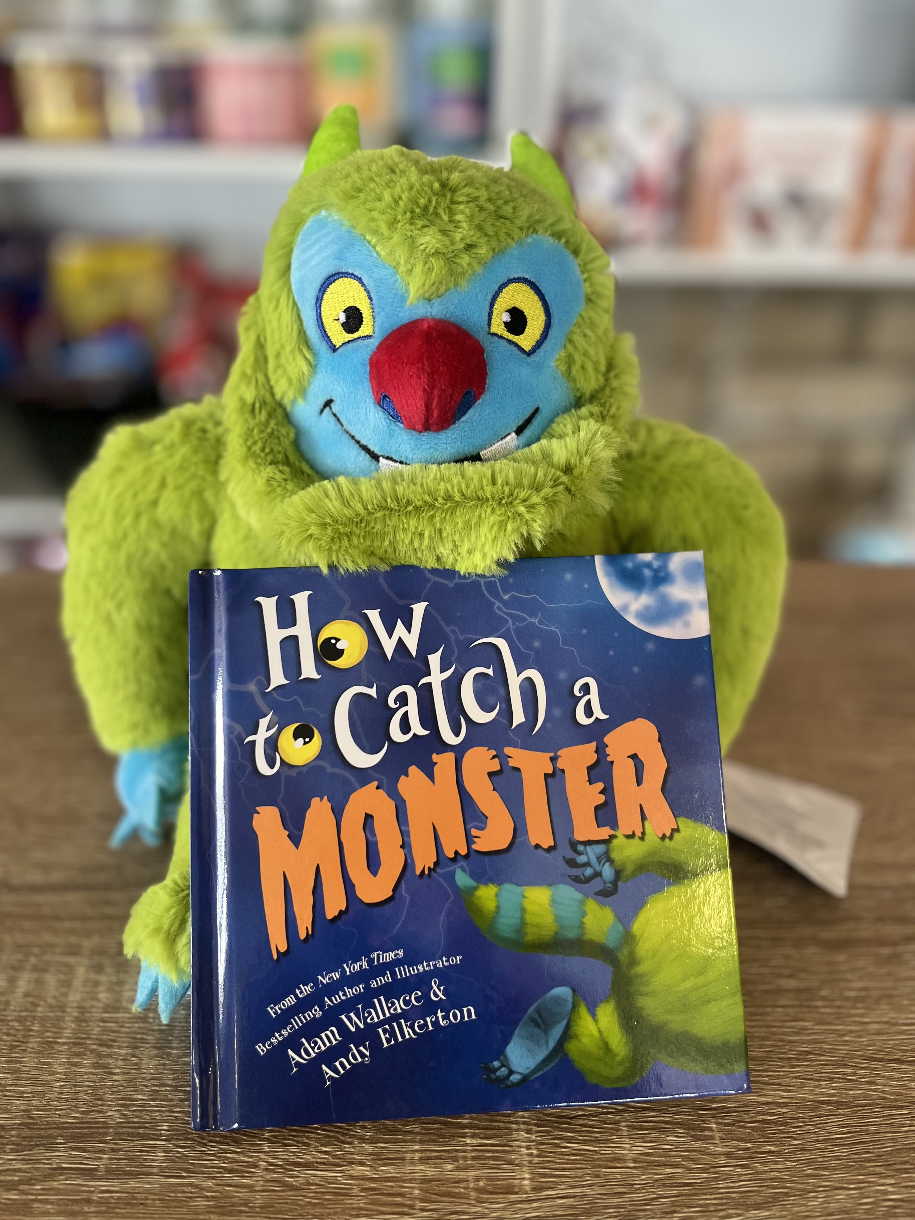 A green plush monster holding a children's book titled "How to Catch a Monster."