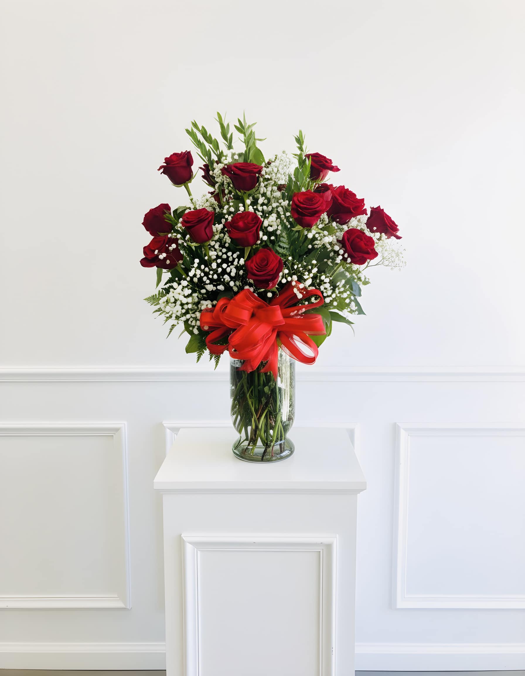 Red roses in a clear glass vase with a red ribbon bow