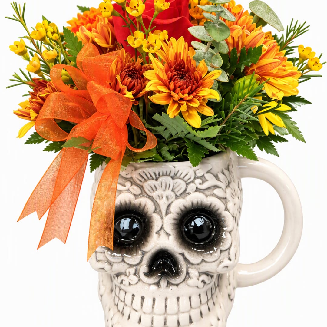 Orange and yellow flowers arranged in a skull-shaped mug with a ribbon