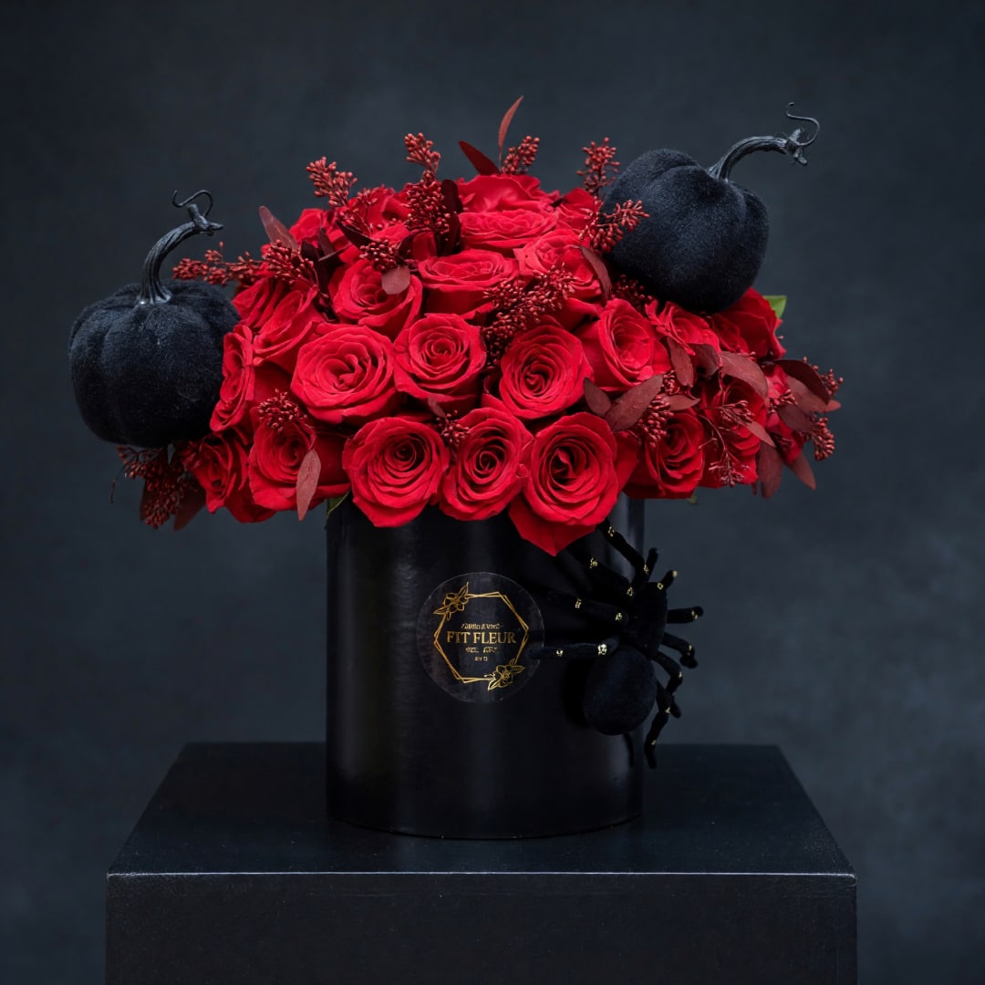 Red roses arranged in a black vase with black pumpkin accents