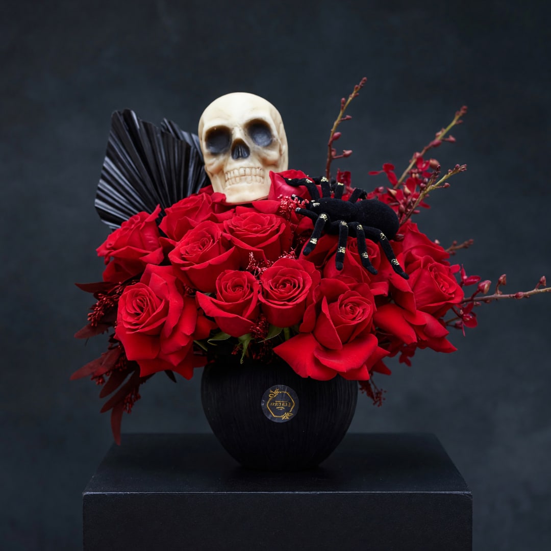 Red roses arranged in a black vase with a skull and spider decoration