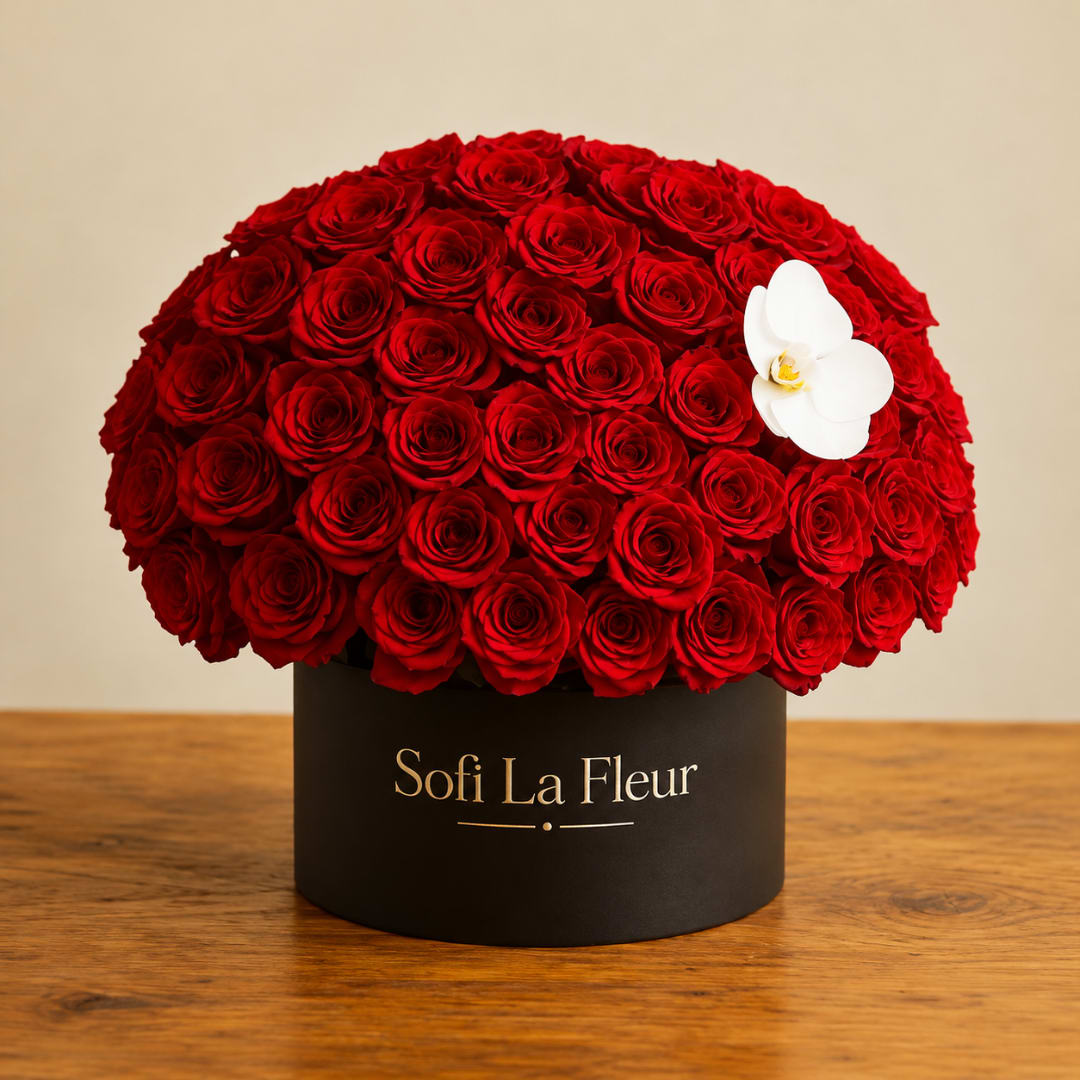 Round arrangement of red roses in a black box with a white orchid accent