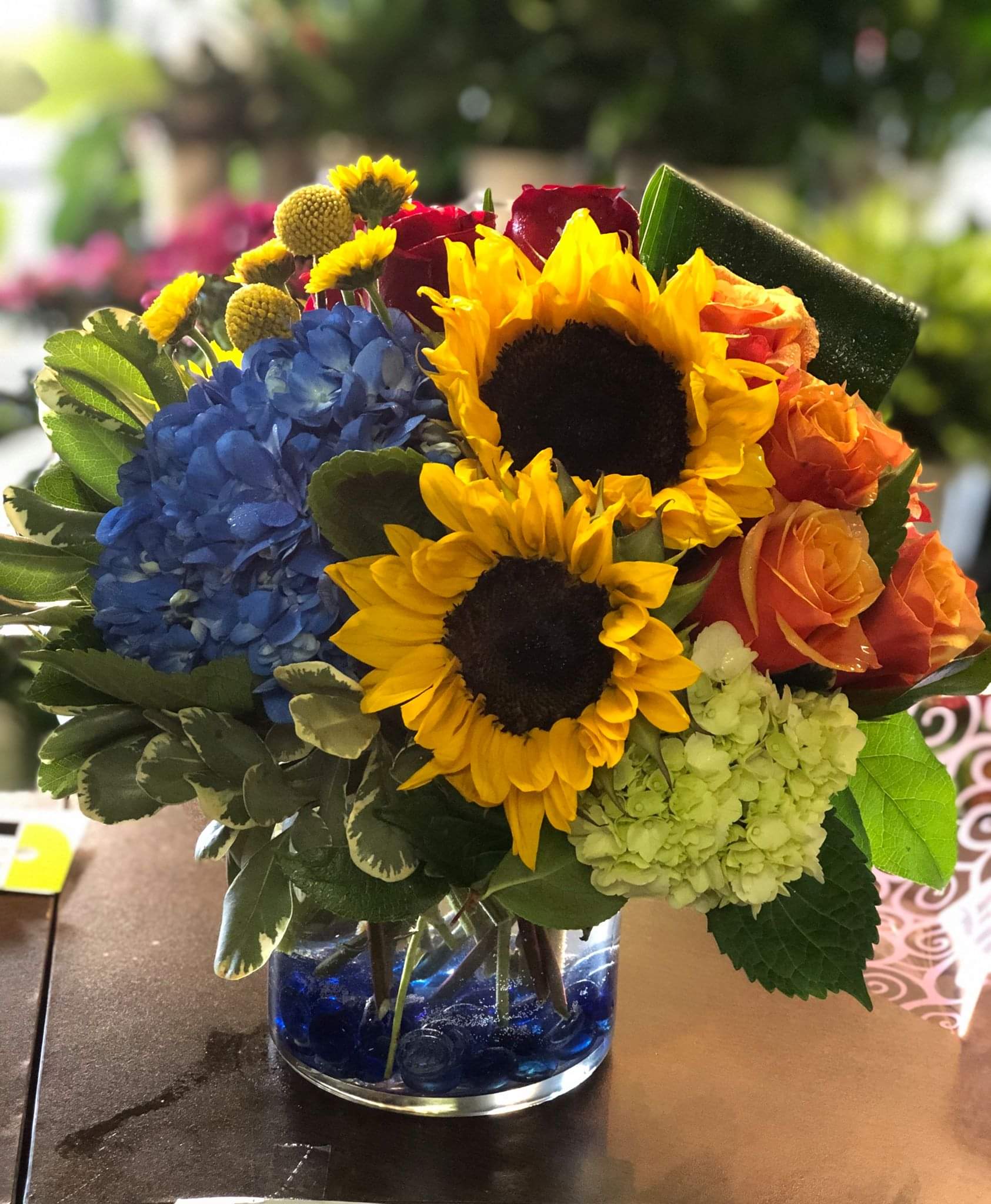 Bouquet with sunflowers, blue hydrangea, and orange roses in a glass vase