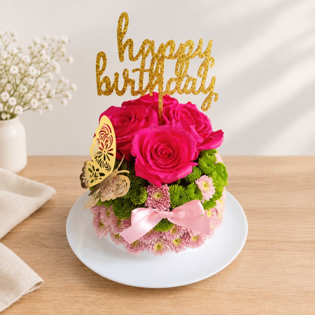 Pink rose arrangement with a gold happy birthday topper on a white plate
