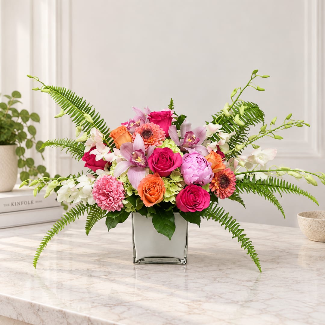 Mixed pink and orange flowers arranged in a square glass vase