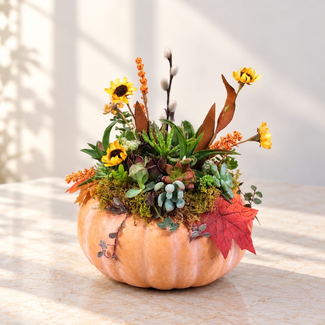Succulent arrangement in a pumpkin with yellow flowers and autumn leaves
