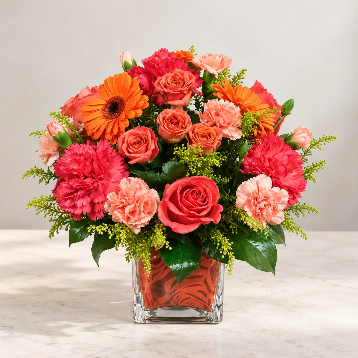 Bright mixed bouquet of roses, gerbera daisies, and carnations in a glass vase