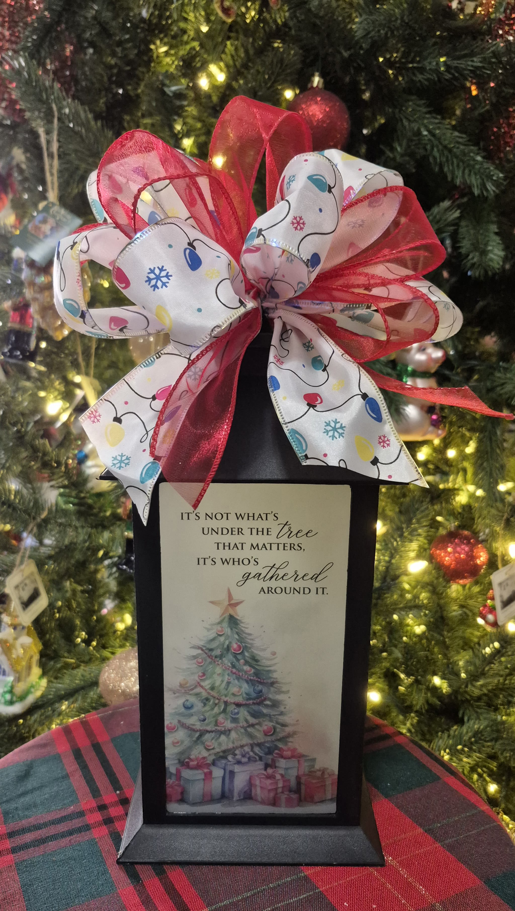Black lantern with a Christmas ribbon bow and holiday card in front of a decorated tree