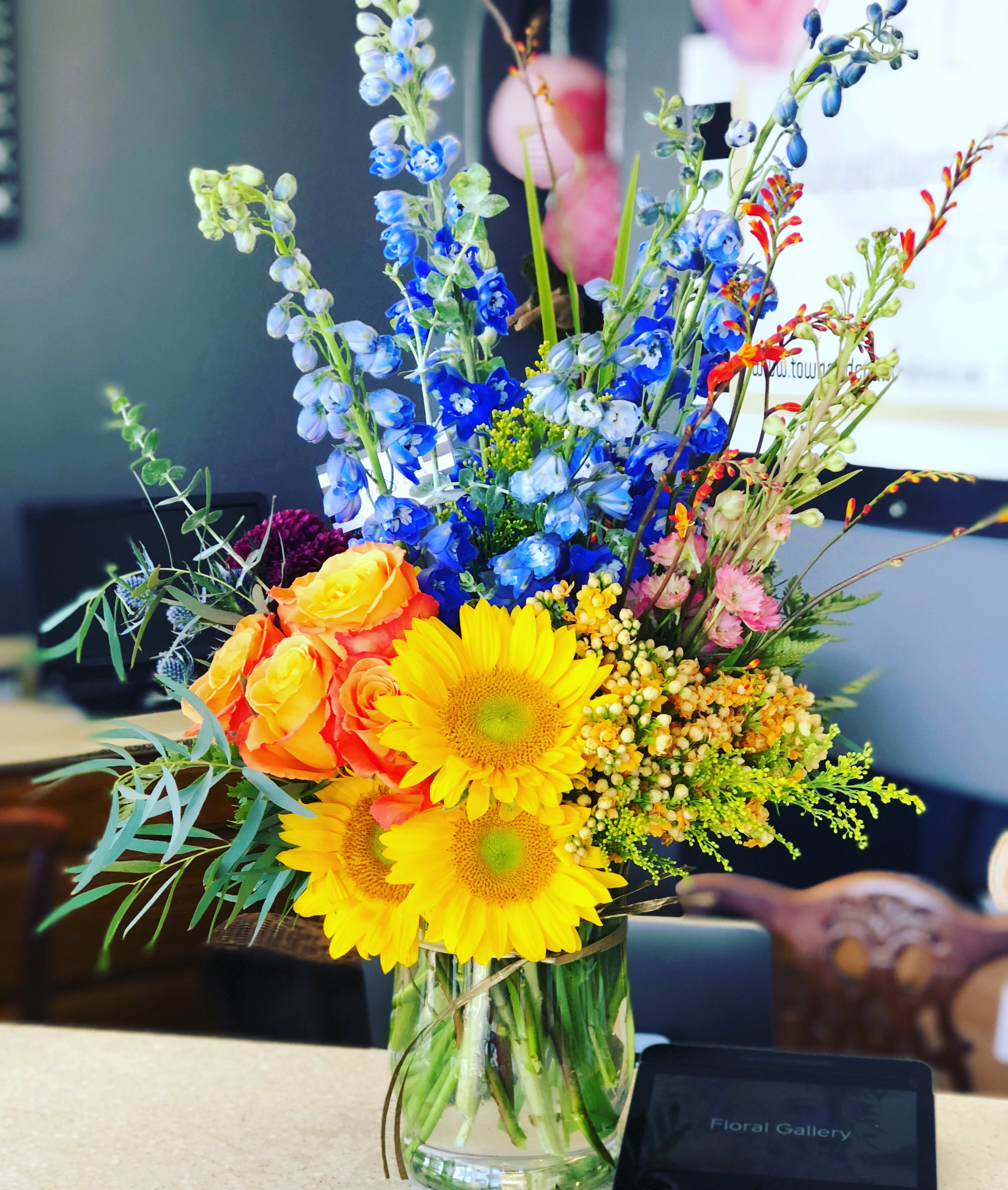 Colorful bouquet with sunflowers, roses, and blue delphinium in a glass vase