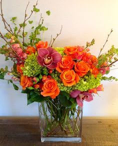 Orange roses and purple orchids in a clear glass vase