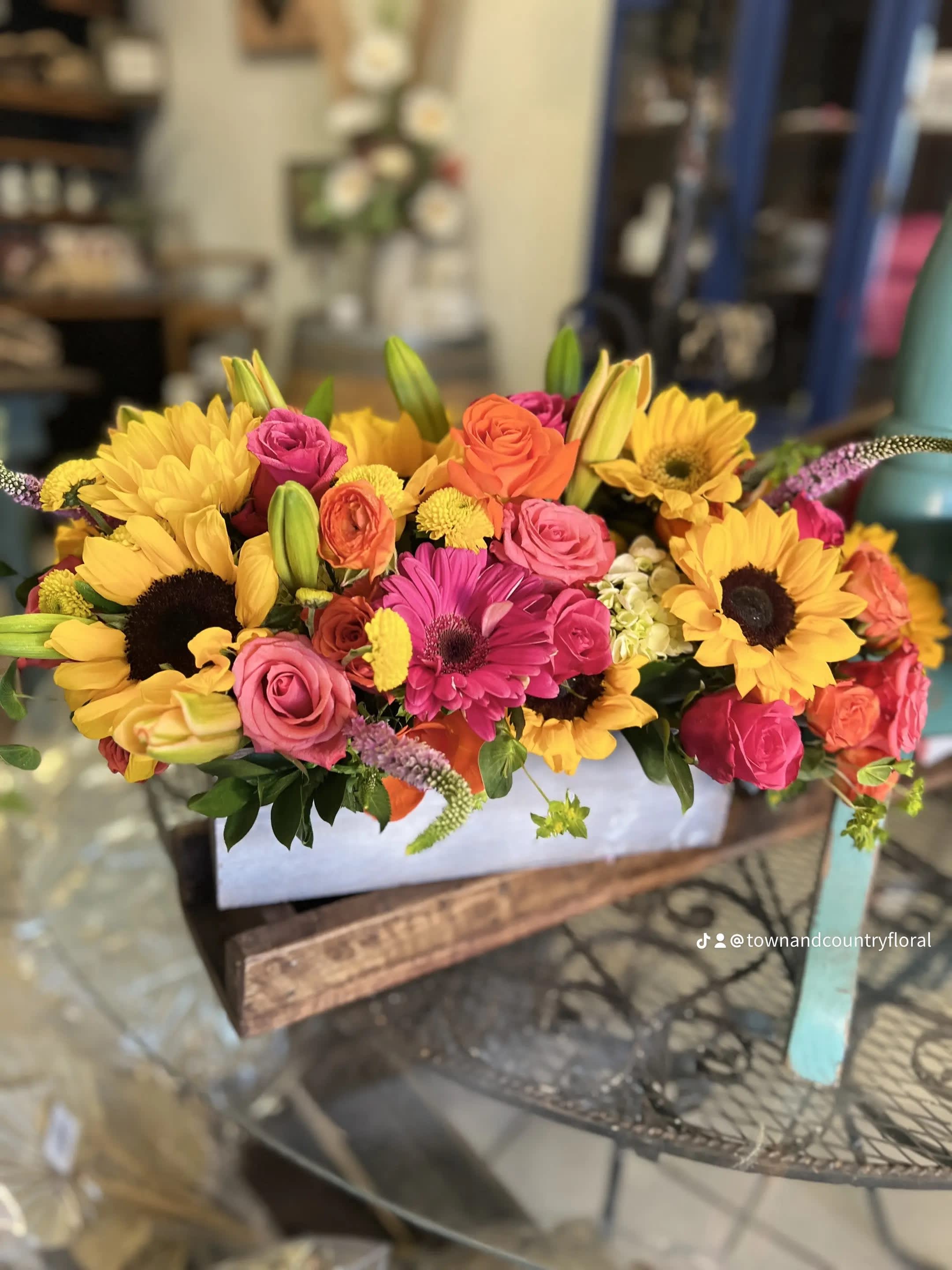 Bright mixed bouquet with sunflowers, roses, and lilies in a white container