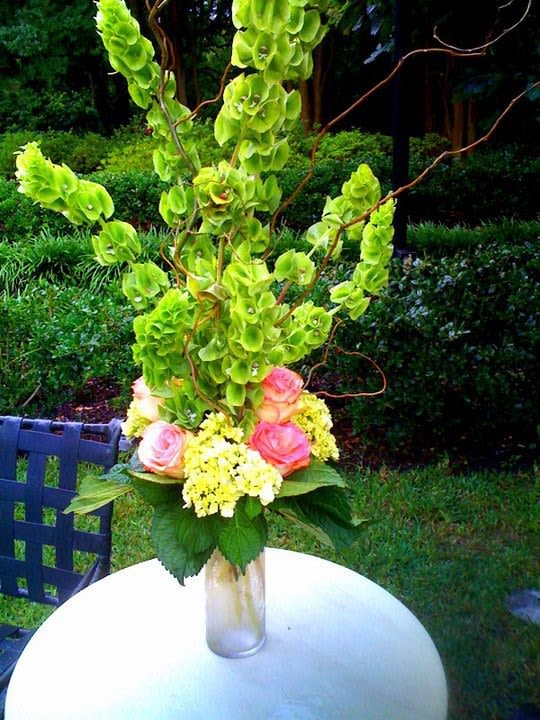 Tall floral arrangement with green orchids and pink roses in a glass vase