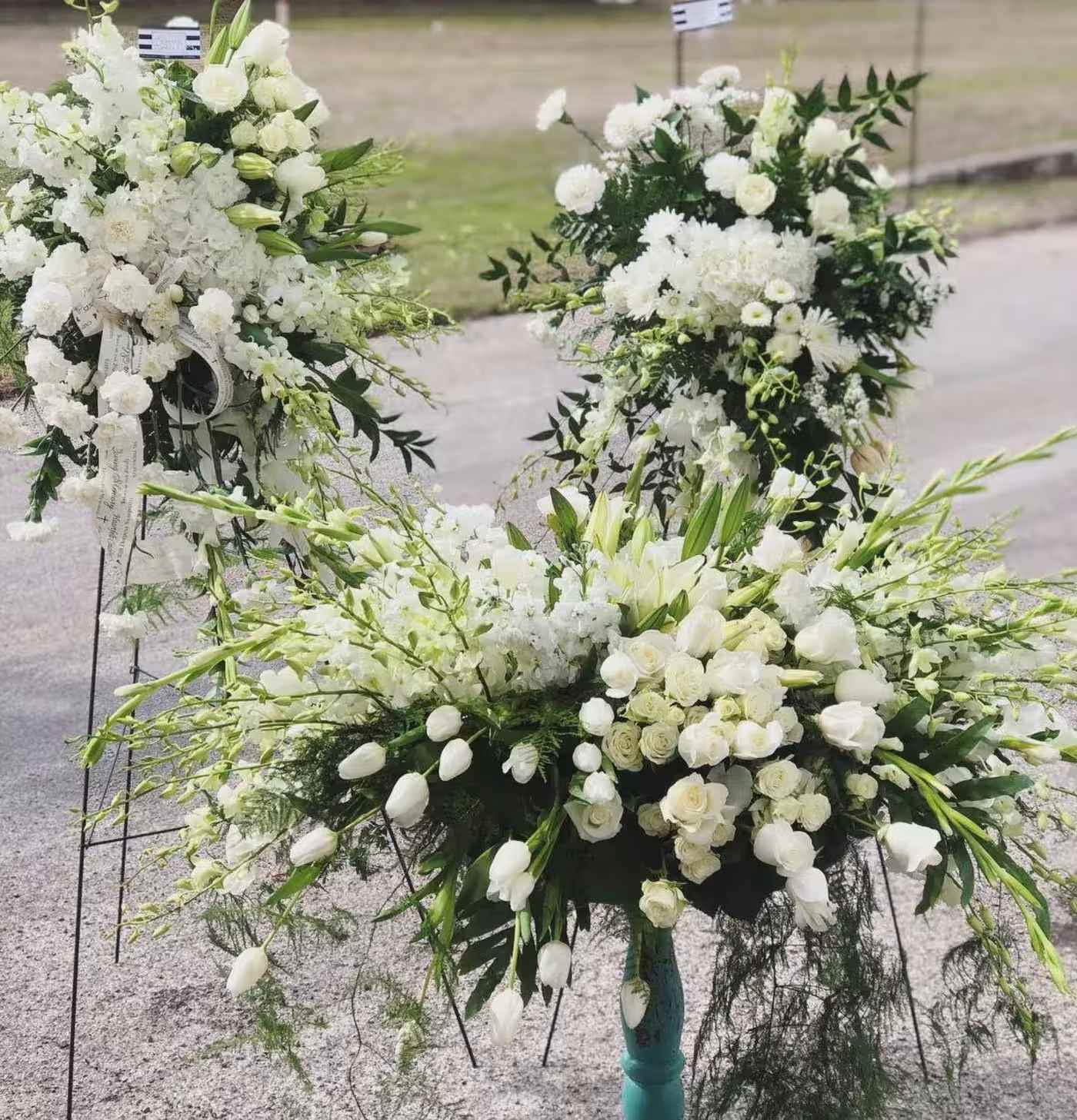 White floral funeral sprays with lilies and roses on stands