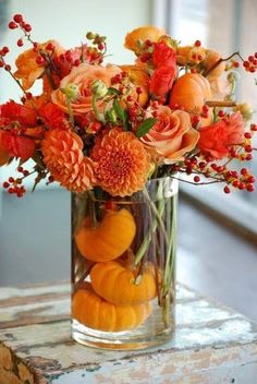 Orange floral arrangement in a clear glass vase with small pumpkins inside