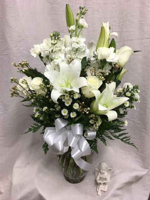 White lilies and roses in a glass vase with a white ribbon