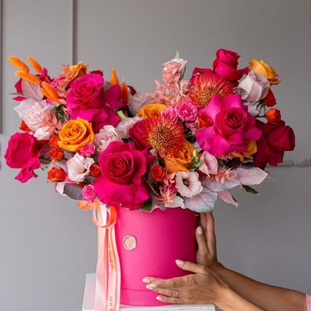 Bright mixed bouquet of roses and orange blooms in a pink hatbox