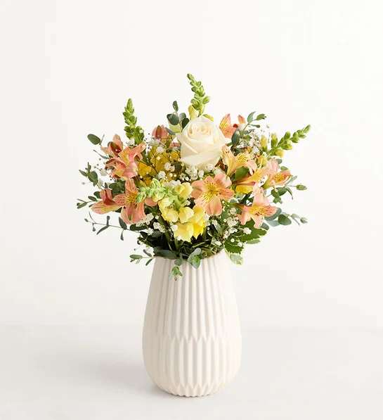 Mixed bouquet of peach and yellow flowers in a white vase