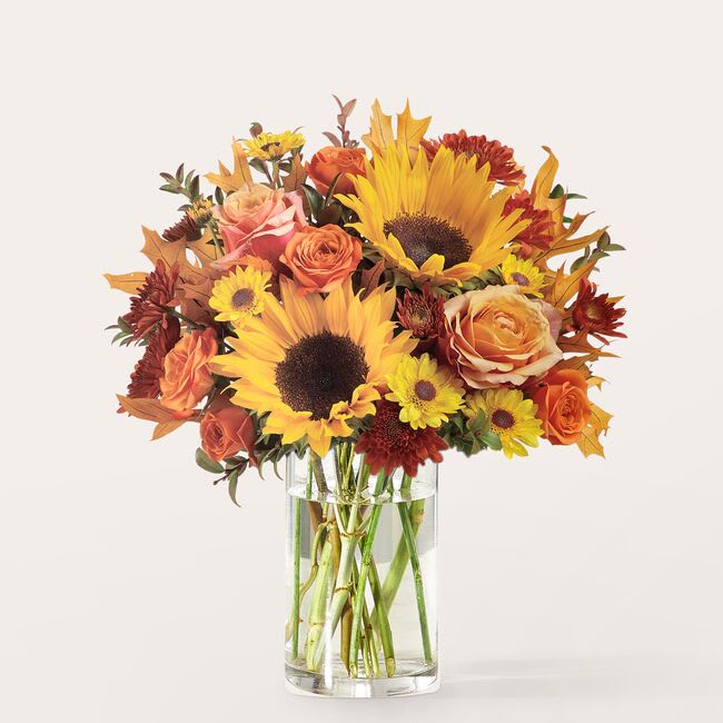 Bouquet of sunflowers, roses, and mums in a clear glass vase