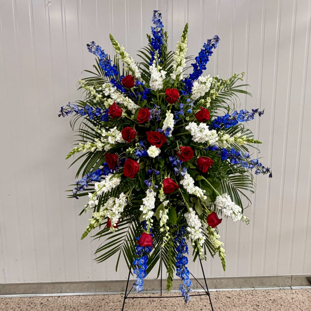 Standing floral spray with red roses, white blooms, and blue flowers