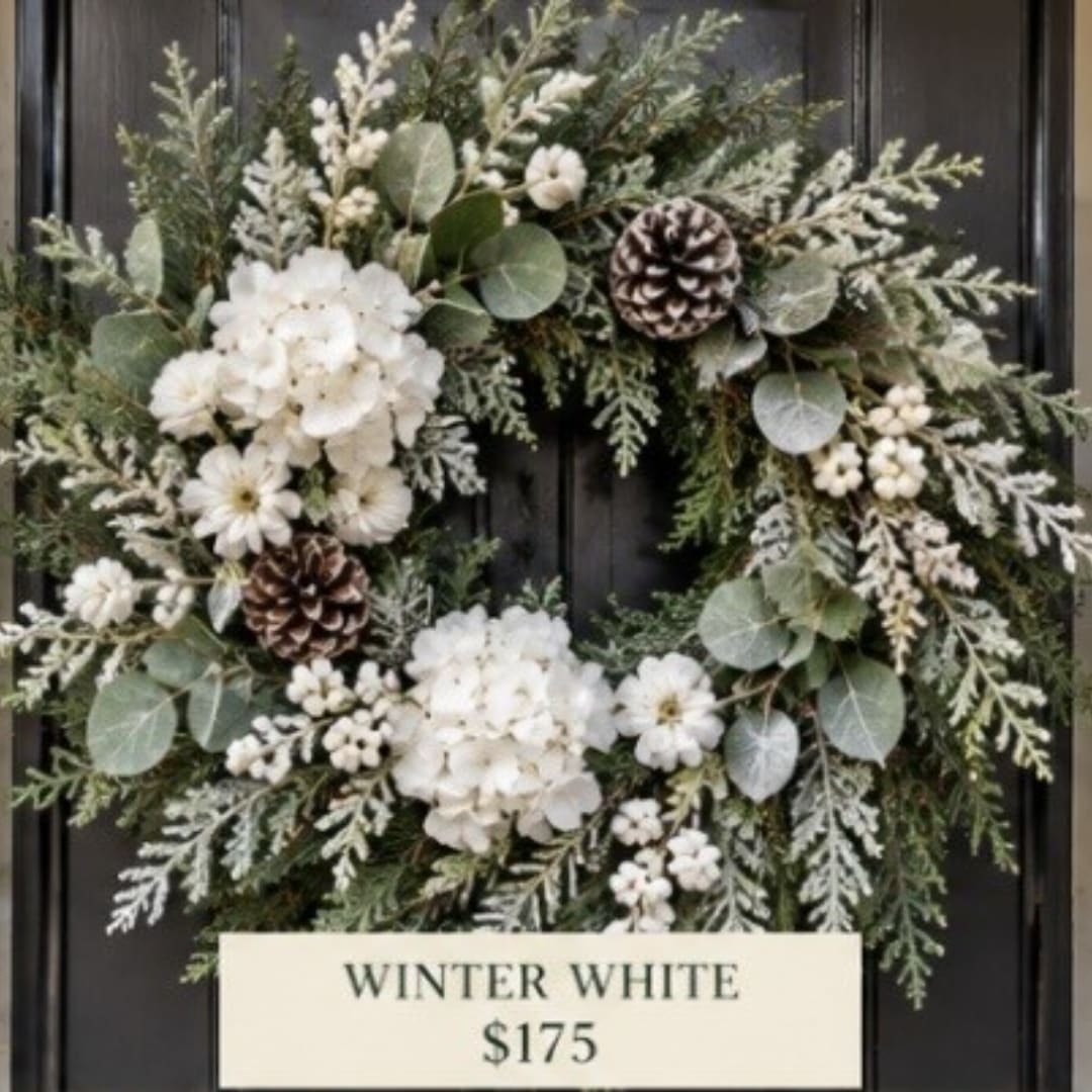 White winter wreath with pinecones and greenery on a dark door