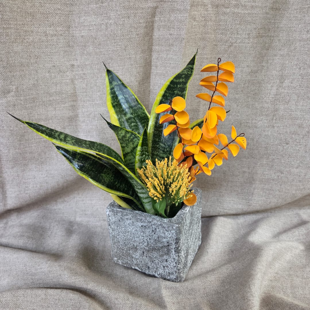 Potted arrangement with snake plant leaves and orange decorative stems in a square planter
