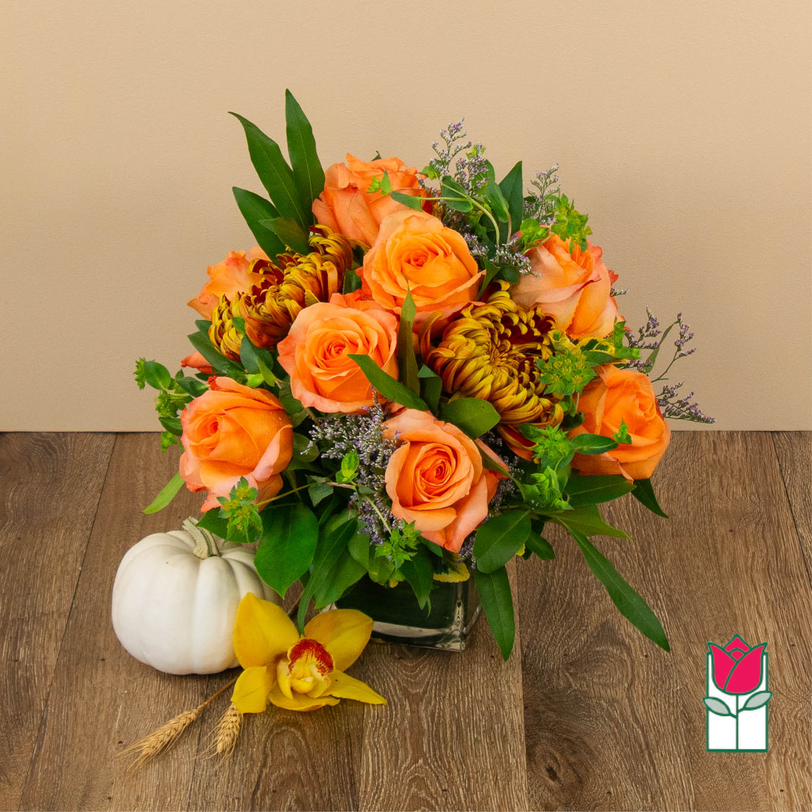 Orange roses and yellow chrysanthemums in a glass vase with a white pumpkin